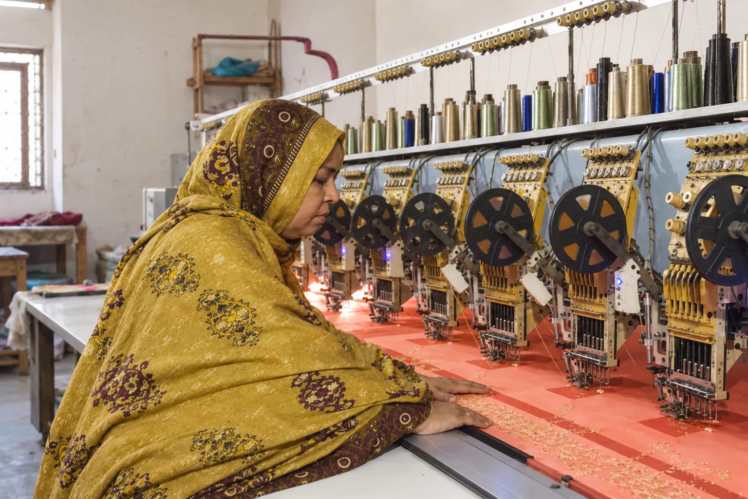 Ruqayya Bibi in her mustard dupatta at the older embroidery machine in her modest workplace